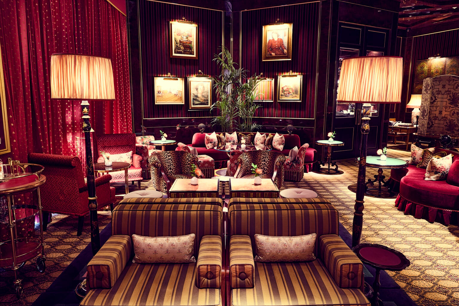 Lounge with red velvet drapes, striped armchairs and framed paintings