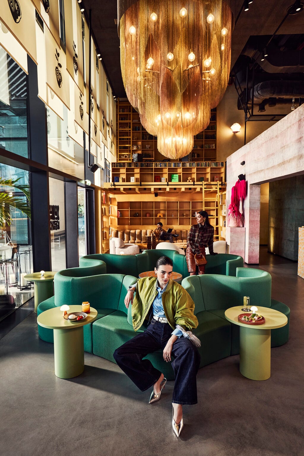 Man relaxing on a curved green sofa beneath a gold chandelier in a double-height lounge