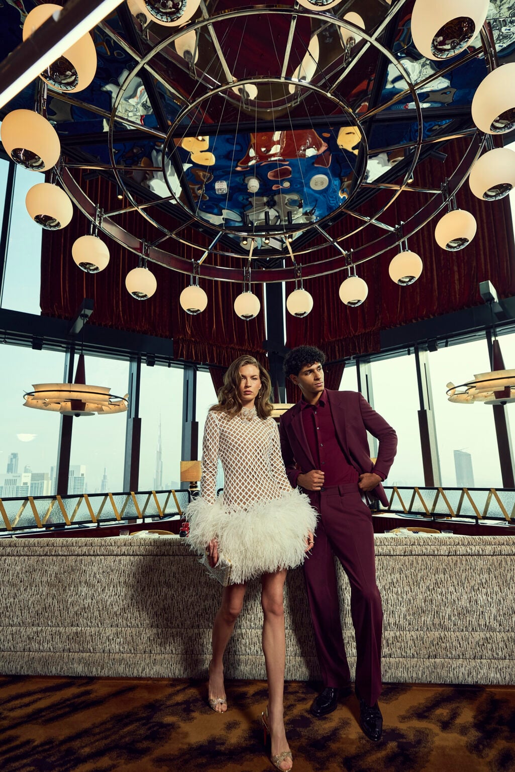 Couple in evening wear beneath a globe-light chandelier in a skyline restaurant