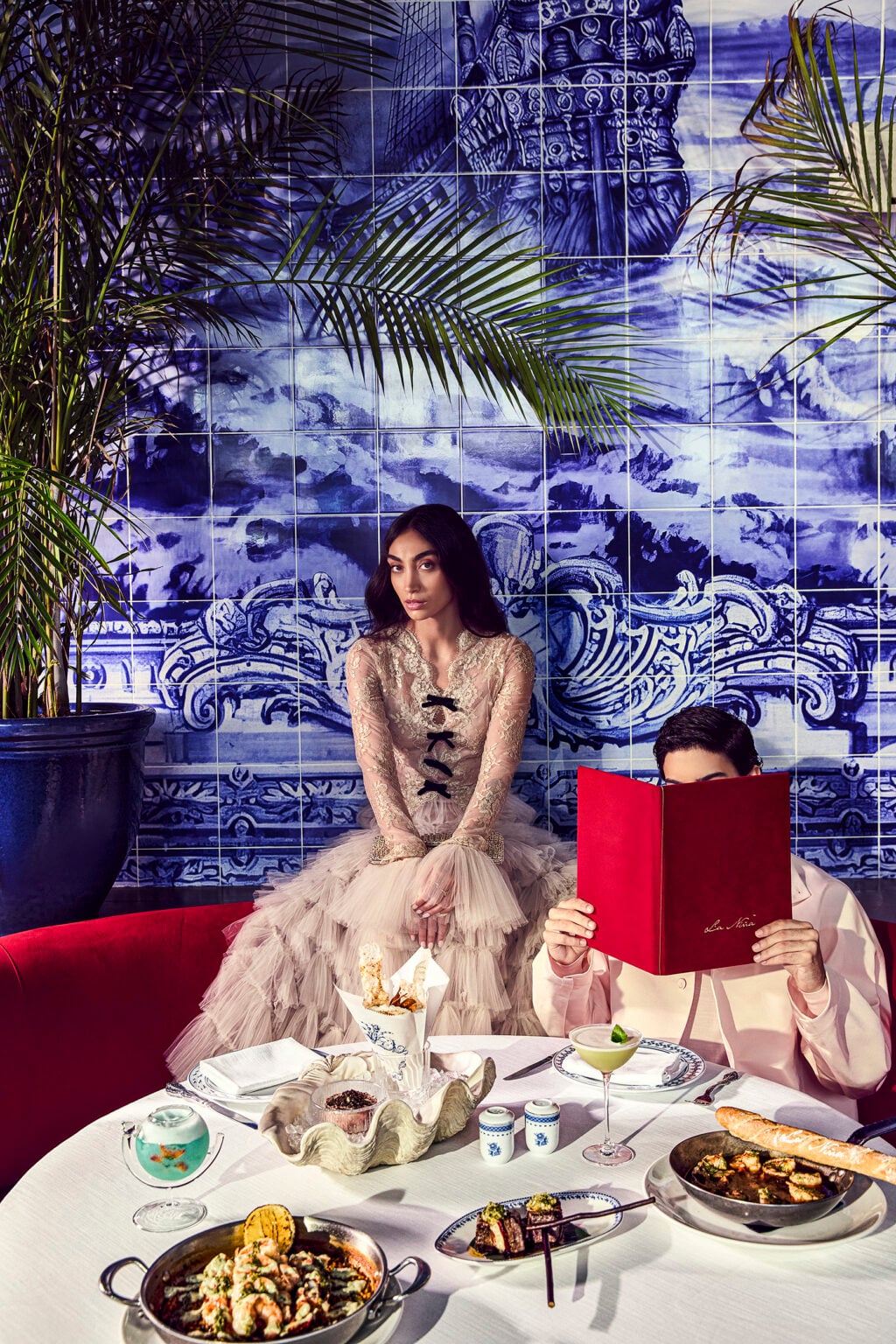 Diners at a restaurant table set with seafood dishes in front of blue and white tiles