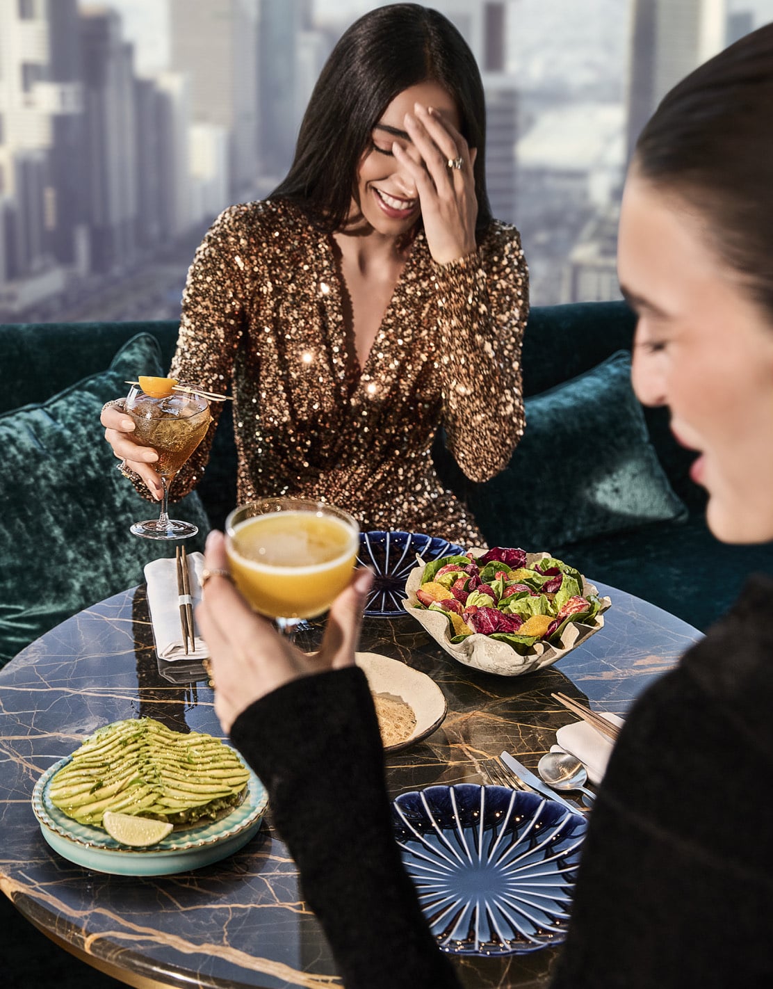 Friends sharing drinks and small plates on a velvet banquette above the Dubai skyline